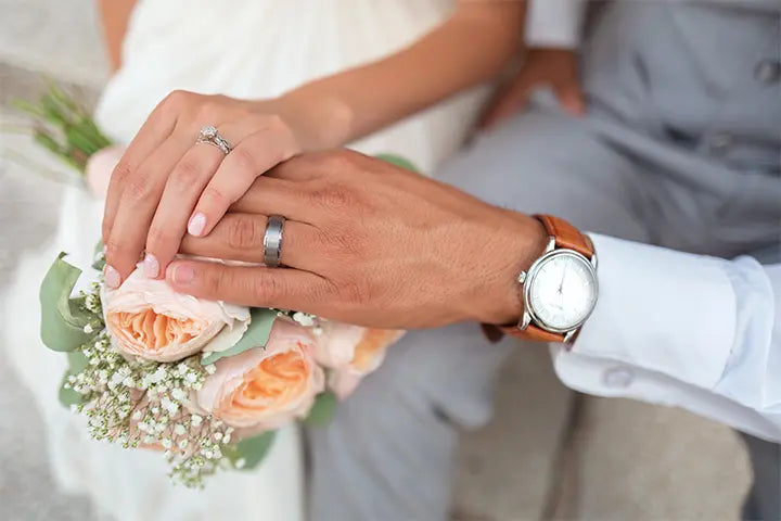Braut und Bräutigam die auf Ihrer Hochzeit Händchen halten. Die Frau hält einen künstlichen Brautstrauß in der Hand.